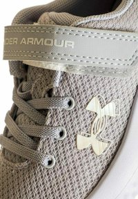 Scarpa sportiva grigia con una tomaia in rete, passanti per i lacci e un accentuato logo bianco. Presenta una cinghia grigia con un branding discreto.