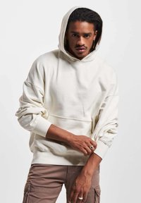 Krèmfarga pullover hettegenser med en stor hette, ribbede mansjetter og en frontlomme. Har en avslappet passform og synlige sømdetaljer.