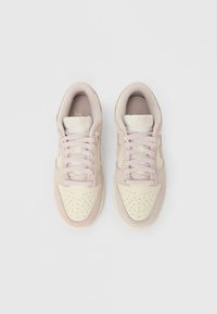 Pár světle růžových a krémových tenisek Nike se šňůrkami, pohled shora na bílém pozadí.