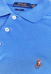 Polo di colore azzurro chiaro realizzato in cotone morbido, con uno scollo a tre bottoni e un logo ricamato di un cavallo e cavaliere in dettagli colorati.