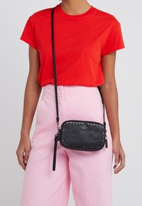 Borsa a tracolla in pelle nera con borchie multicolore lungo i bordi. Dotata di tracolla removibile e chiusura con zip. Design compatto e rettangolare.