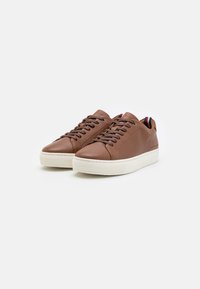 Sneaker in pelle marrone con superficie testurizzata, suole in gomma bianca e lacci piatti. Presenta un accento a righe sul tallone.
