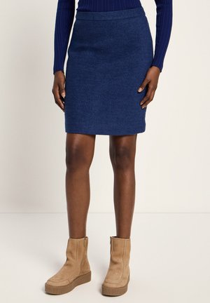 Frau trägt einen knielangen Rock in Marineblau, ein marineblaues, geripptes Langarmshirt und beige Wildleder-Paa-Plateau-Stiefeletten.