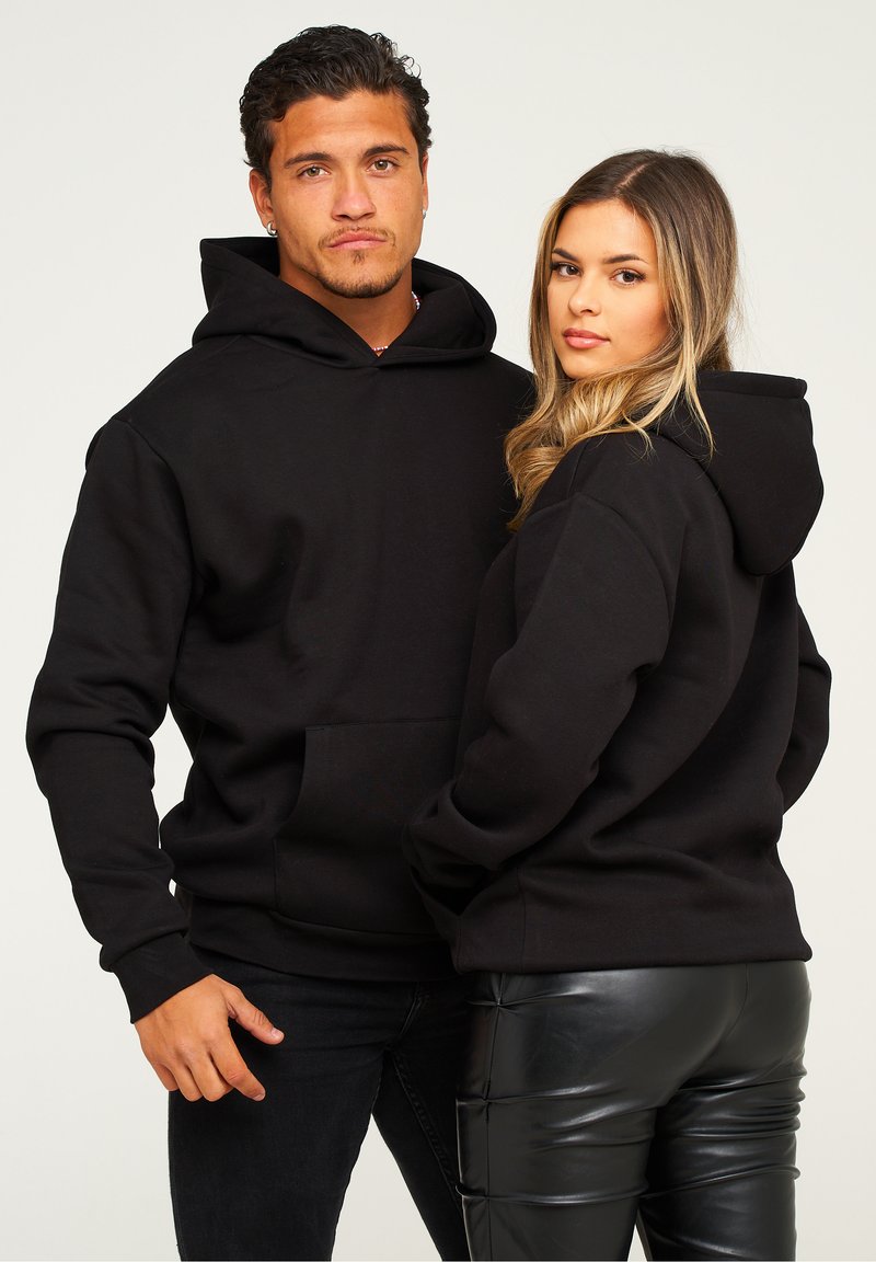 Schwarze Hoodies mit Fronttaschen, aus einem weichen Stoff gefertigt. Mit langen Ärmeln und einer lockeren Passform, präsentiert von zwei Personen vor einem neutralen Hintergrund.