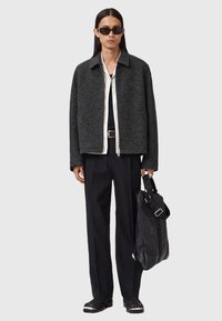 Donker wollen jasje met een spread collar, ritssluiting, gelaagd over een wit shirt, gecombineerd met zwarte broek en een gestructureerde zwarte tas.