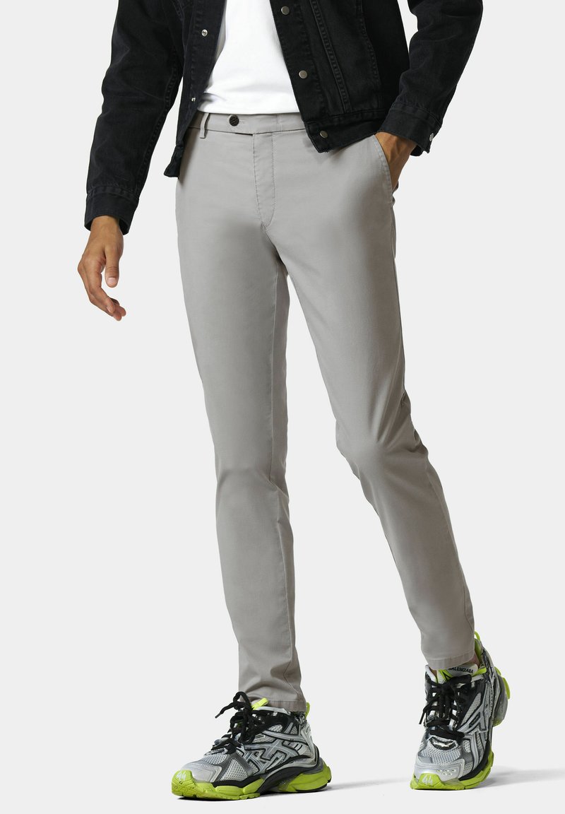 Graue Tailor-Pants in schlanker Passform, aus glattem Stoff. Kombiniert mit schwarzen Sneakers mit leuchtend grünen Akzenten.