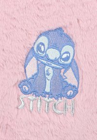 Rosa plysht stof med en broderet blå karakter med store øjne og teksten "STITCH" nedenfor i sølvtråd.
