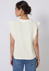 Hvid kortærmet top i et blødt, tekstureret stof med en afslappet pasform, der har flæse detaljer på skuldrene. Sammen med højtaljede jeans.