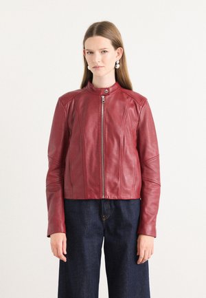 Red leather cropped jacket with a stand collar, front zip closure, and detailed stitching on sleeves. Worn over dark denim pants.