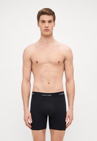 Fekete pamut boxer alsónadrág, puha tapintással és illeszkedő elasztikus derékkal, amelyen fehér színű "Calvin Klein" logó található.