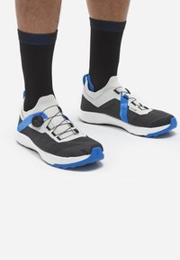 Czarno-białe sportowe buty z niebieskimi akcentami, cechujące się opływowym kształtem, teksturowanym materiałem oraz systemem szybkiego sznurowania BOA.