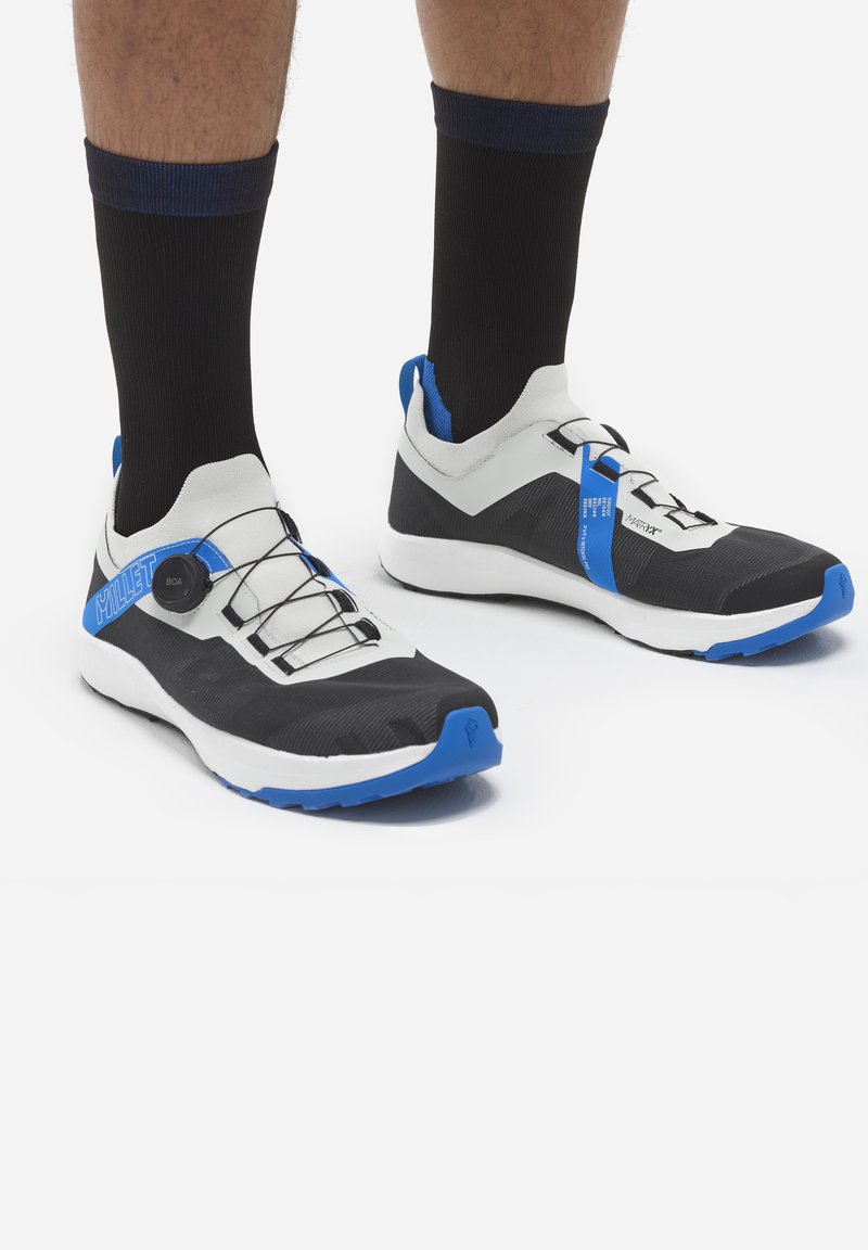 Czarno-białe sportowe buty z niebieskimi akcentami, cechujące się opływowym kształtem, teksturowanym materiałem oraz systemem szybkiego sznurowania BOA.