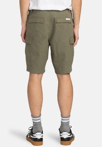 Pantalones cortos cargo de color verde oliva con doble bolsillo lateral, bolsillos traseros y un corte relajado. Combinados con zapatillas negras y blancas y calcetines grises.