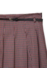 Jupe à motif pied-de-poule en rouge, noir et blanc avec des plis et une ceinture noire équipée d'une boucle argentée. Tissu texturé.