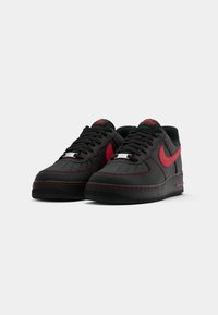 Black sneakers with red accents, leather upper, perforated toe box, and black rubber sole. Features red stitching and signature branding.