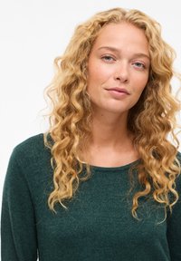 Maglione verde a maglia texturizzata con scollatura rotonda. Il design presenta maniche lunghe e una vestibilità rilassata. Indossato da una persona con capelli mossi.