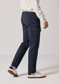 Navy cargo pants feature side pockets, a relaxed fit, and a lightweight fabric. Worn with white sneakers and a light sweater.