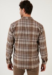Camicia di flanella a quadri in marrone e crema, con maniche lunghe, polsini con bottoni e una vestibilità rilassata; presenta un motivo tessuto e strutturato.