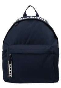 Sac à dos bleu marine avec poche zippée à l'avant, poignée noire, logo Timberland blanc sur le bord supérieur et tirette de fermeture éclair marquée.