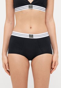 Svart boxertrosor med en vit randig elastisk midjeband och en logotyp-patch. Mjukt, stretchigt tyg med sömdetaljer.