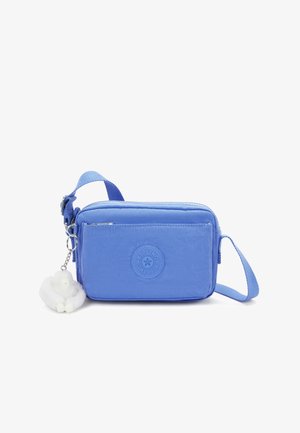 Blue nylon crossbody bag with a front pocket, adjustable strap, and a white fur charm. Features a circular logo embossed on the front.
