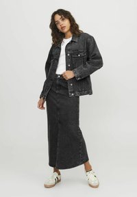 Zwarte denimjas met knoopsluiting, gecombineerd met een zwarte denim maxi rok. Witte t-shirt eronder en witte sneakers met bruine accenten.