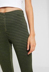 Gröna rutig högmidjade byxor med dragkedja fram och metallringdetalj, tillverkade av ett texturerat tyg med slim fit.