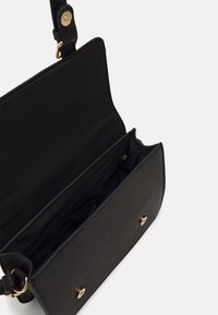 Černá crossbody taška vyrobená z hladkého materiálu, se skládacím víkem a zlatým kováním, zipovou kapsou a dvojitými vnitřními přihrádkami.