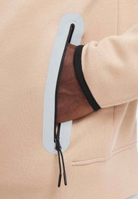 Felpa beige con una grande tasca con zip grigia lungo la manica. Accento nero al polsino e tessuto testurizzato visibile.