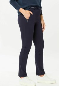 Marineblauwe stretchbroek met een slim fit, voorzien van een zijrits zak en een contrasterende tailleband. Gecombineerd met witte platform sneakers.