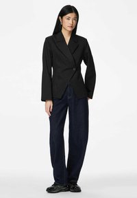 Czarna marynarka w cienkie prążki z notched klapami, dopasowany krój, pojedyncze zapięcie na guzik, zestawiona z szerokimi ciemnymi dżinsami i czarnymi tenisówkami.