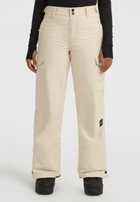 Beige sneeuwbroek met cargozakken, verstelbare tailleband en drukknoopsluitingen. Gemaakt van een gladde stof; past over zwarte winterlaarzen.