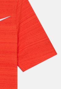 Camisa deportiva corta roja de manga corta con tela texturizada y un logo de Nike en blanco en el pecho. El diseño cuenta con un cuello redondo.