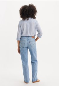 Jeans de pierna recta en azul claro con un parche de cuero trasero y costuras en contraste. Combinados con una camisa a rayas azul y blanca, de estilo casual.