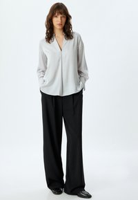 Zijdeachtige lichtgrijze blouse met een V-hals en lange mouwen, gecombineerd met zwarte hoogwaisted wijde broek en glanzende zwarte schoenen.
