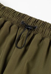 Elastyczny pasek w oliwkowym kolorze z marszczonym nadrukiem. Posiada czarny sznurek do regulacji oraz metalowe oczka.