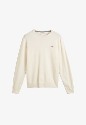Crème-kleurige gebreide trui met lange mouwen en een ribgebreide onderrand, met een klein geborduurd logo op de borst. Soepele textuur.