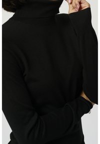 Czarny dzianinowy golf, dopasowany krój, długie rękawy, prążkowana faktura na kołnierzu i mankietach, widok z bliska.