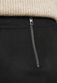 Svart mockaskirt med en silverdragkedja framtill. Slät textur, figurnära design med subtila sömnadsdetaljer.