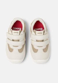 Weiße und beige Kindertrainingsschuhe mit Klettverschlüssen, strukturiertem Stoff und rotem Innenfutter, auf dem der Markenname "CAMPER" in Weiß zu sehen ist.
