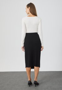 Un top alb cu mâneci lungi, băgat într-o fustă midi neagră cu textură ribbed, având un croi ajustat pe talie și o slit lateral. Pantofii cu toc negri completează look-ul.