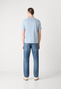 Lys blå kortermet t-skjorte kombinert med rette blå jeans, med baklommer og et enkelt design. Hvite sko fullfører antrekket.