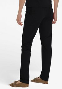 Zwarte op maat gemaakte broek met een soepele textuur, voorzien van een middelhoge taille, zijzakken en een slim fit, in combinatie met bruine loafers.