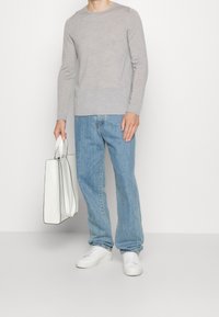 Ljusgrå tröja av mjukt material, tillsammans med ljusblå jeans. En vit tote-väska med svarta detaljer hålls i ena handen.