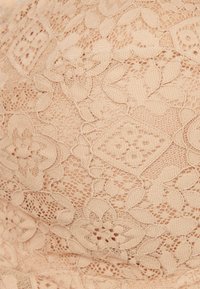 Nude koronka z kwiatowymi wzorami, z misternymi detalami i teksturami, prezentująca delikatny i lekki design.