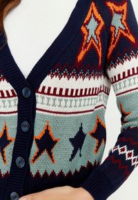 Strickjacke mit navy Grundfarbe und mehrfarbigen Sternmustern, Knopfverschluss und gerippten Bündchen. Aus weichem Garn gefertigt.