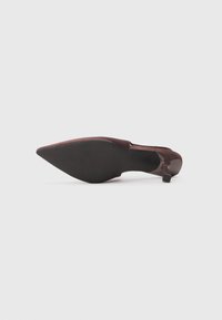 Shoe castanho de biqueira em ponta com um salto baixo, apresentando um cabedal em couro envernizado liso e uma sola de borracha texturizada.