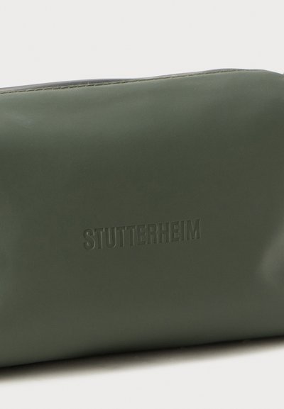 Borsa verde, con texture liscia e il logo "STUTTERHEIM" in rilievo. Forma rettangolare e chiusura con zip, design minimale senza motivi.