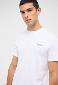 Biały bawełniany t-shirt z krótkim rękawem i okrągłym dekoltem. Na lewej stronie klatki piersiowej znajduje się małe czarne logo "MUSTANG".