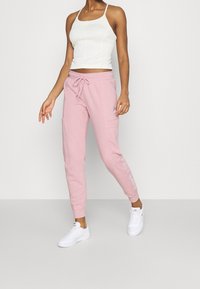 Rosa bomullssweatpants med elastisk midja och dragsko. Sidofickor och logodetalj på benet. Kombinerad med en vit linne och sneakers.